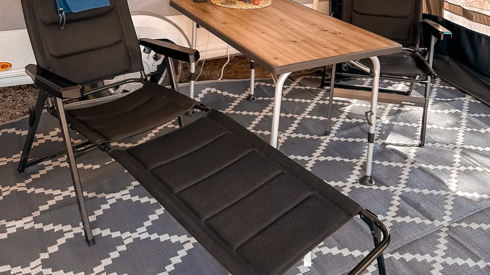 Campingstühle mit Beinauflage und Tisch auf einem Teppich im Vorzelt