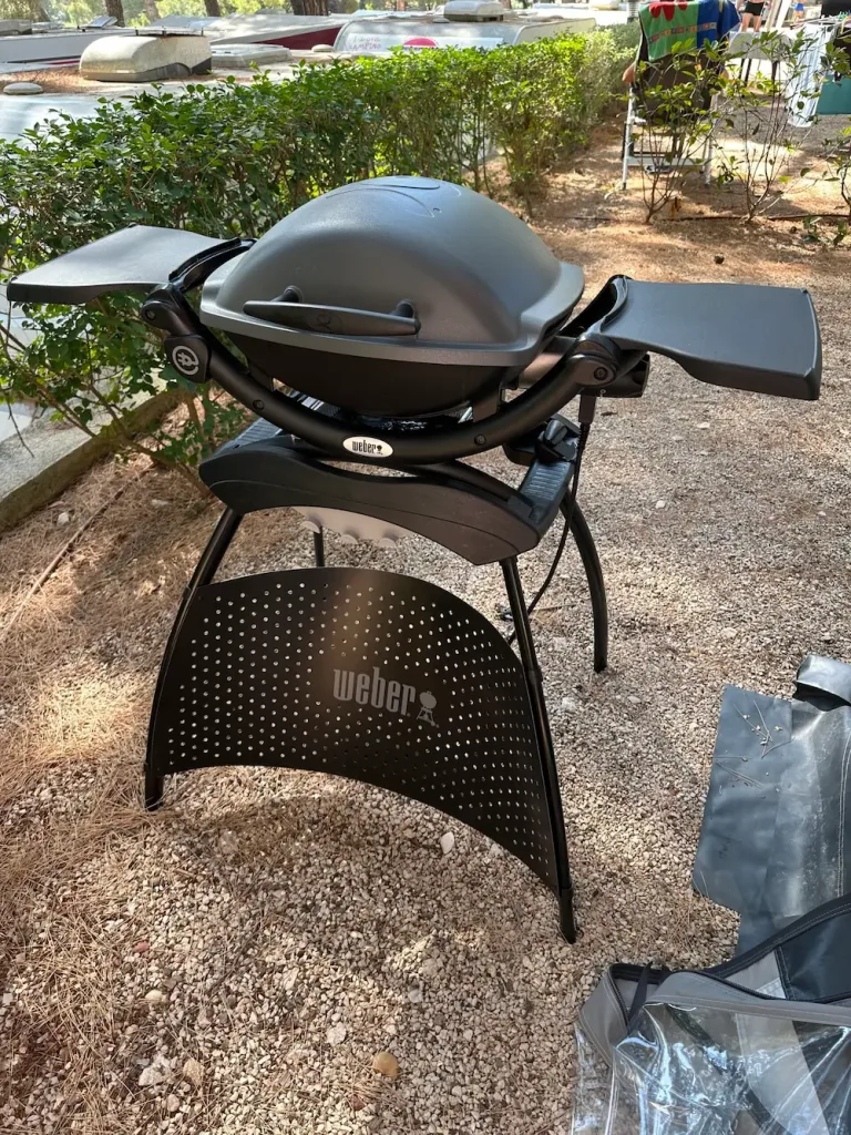Weber Q1400 beim Camping am Stellplatz in Betrieb; Gussrost, Stromkabel, sauberes Branding – passend für 10-A-Anschluss