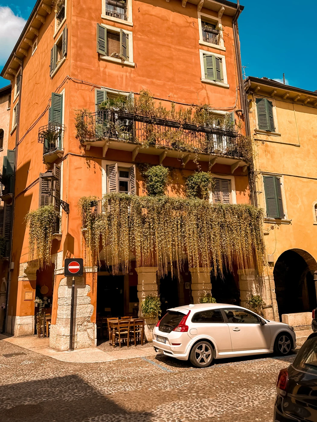 Ockerfarbenes Altstadthaus in Verona mit Laubengang, grünen Fensterläden und bewachsenem Balkon.