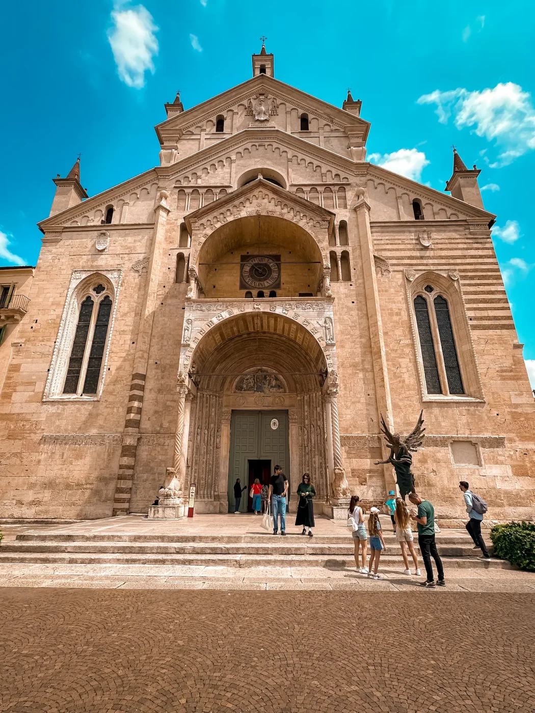 Hauptportal des Duomo di Verona mit romanischem Bogenvorbau, Löwenfiguren und Besucher:innen auf den Stufen