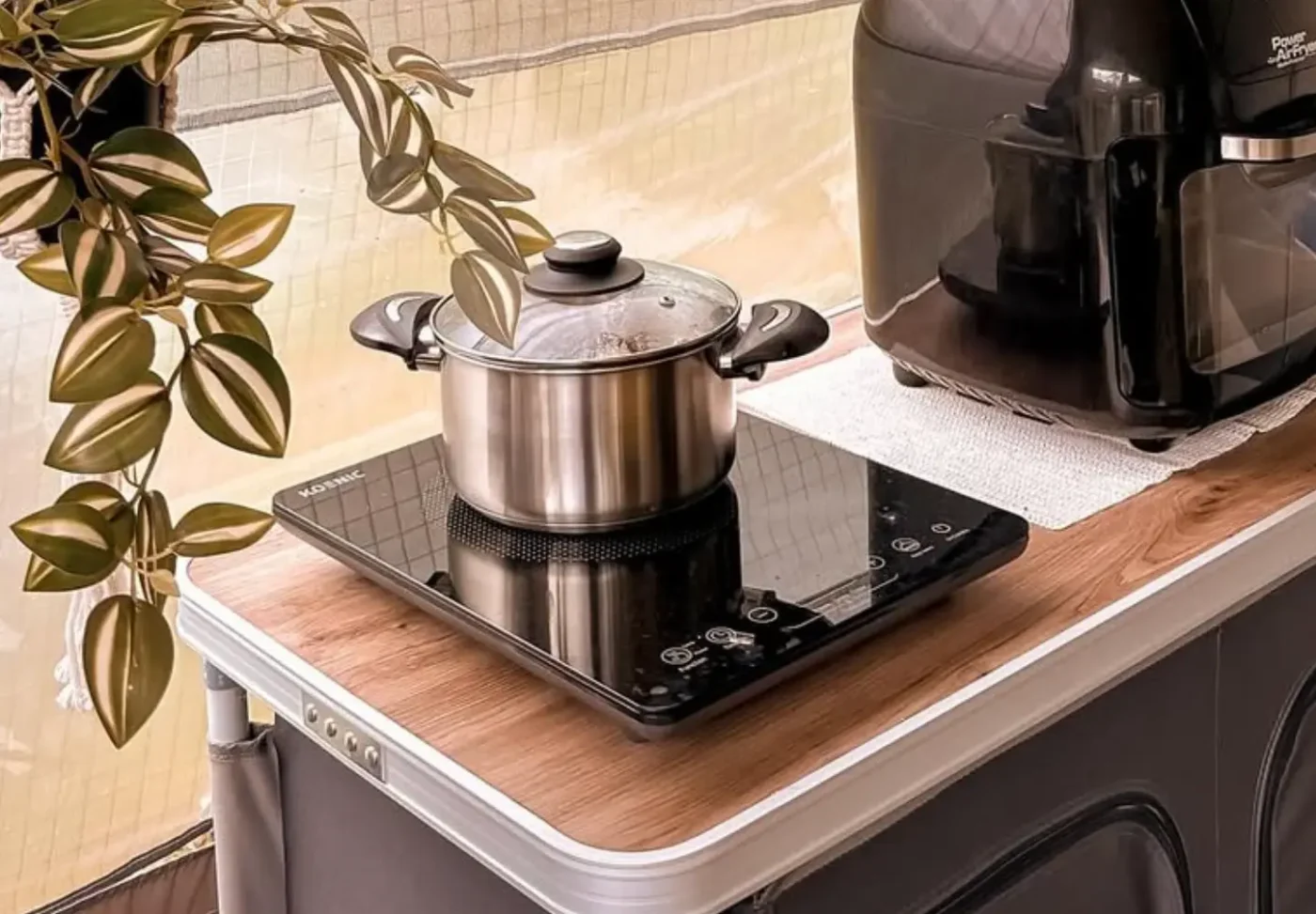 Camping Gadgets: Induktionskochplatte mit Kochtopf auf Holzoptik-Campingschrank – leises, energiesparendes Kochen beim Camping