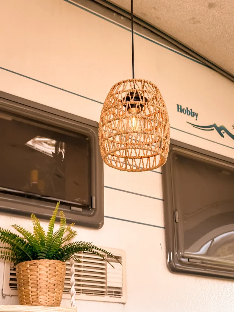Boho-Licht im Caravan: Rattan-Pendelleuchte über Regal mit Pflanze – Inspiration für Weihnachtsgeschenke für Camper.