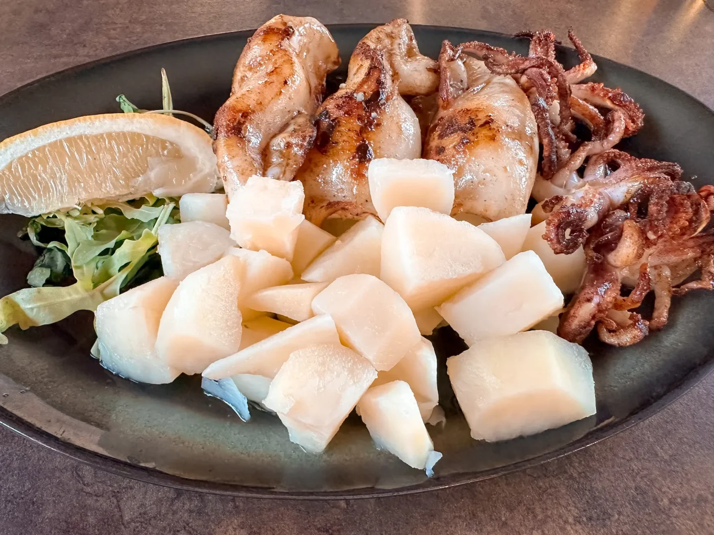 Gegrillte Calamari mit Kartoffeln, Salat und Zitrone im Restaurant am Strand des Camping Arena Stupice