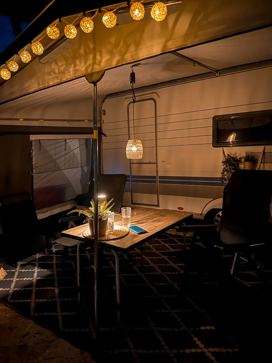 Unser Vorzelt im Camping Arena Stupice bei Nacht mit warmer Lichterkette, Hängelampe, Campingtisch und Wohnwagen