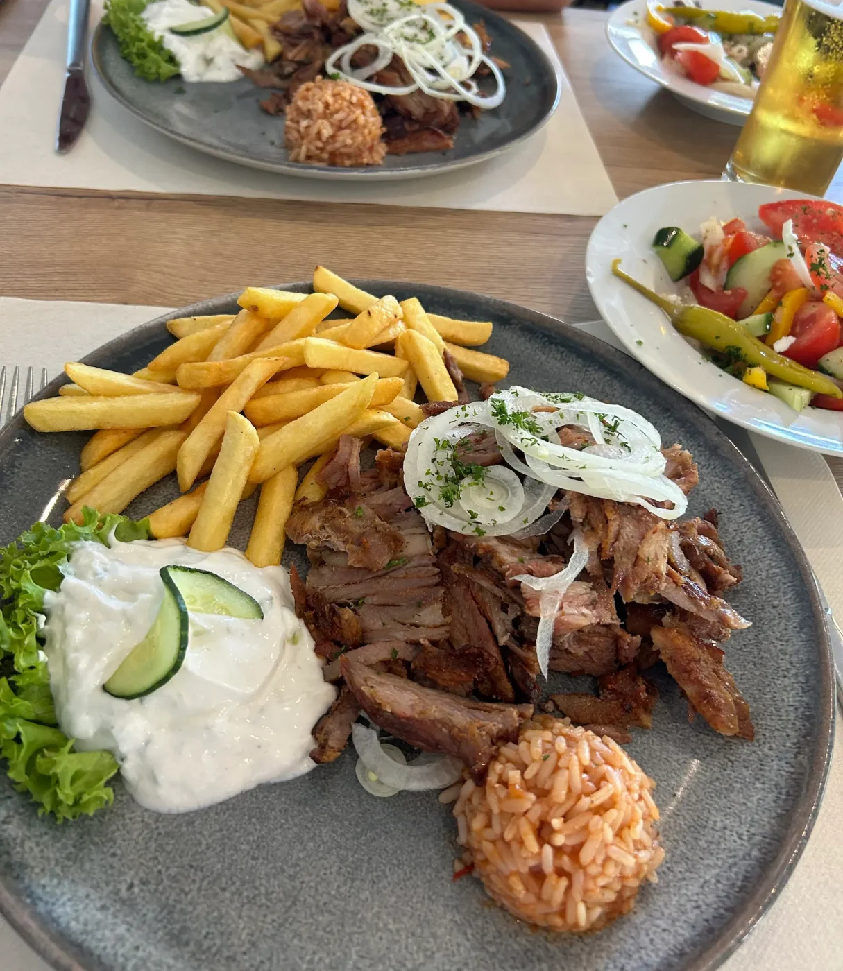 Teller mit Gyros, Pommes, Tzatziki, Zwiebeln und Reis in einem griechischen Restaurant