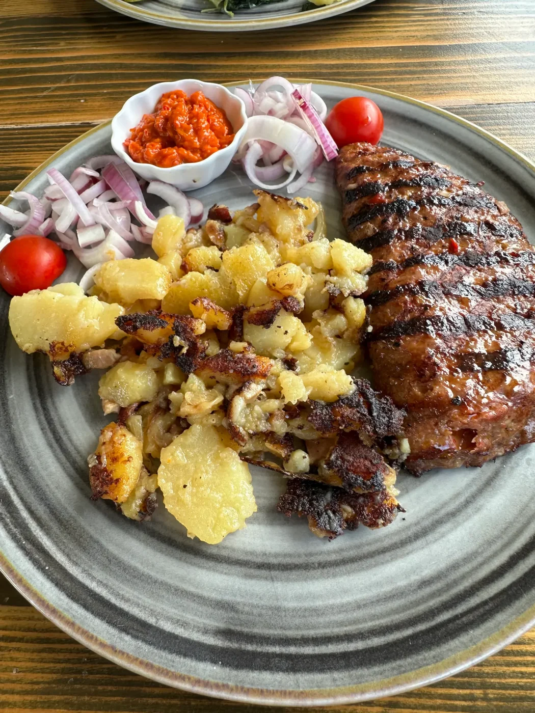Pljeskavica mit Bratkartoffeln, Zwiebeln, Ajvar und Cherrytomaten in der Istarska Farma im Kap Kamenjak