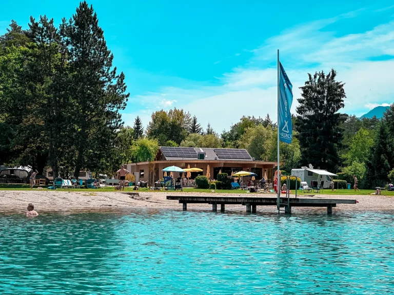 Badesteg, Liegewiese und Gebäude von Strandcamping Gruber am türkisfarbenen Faaker See