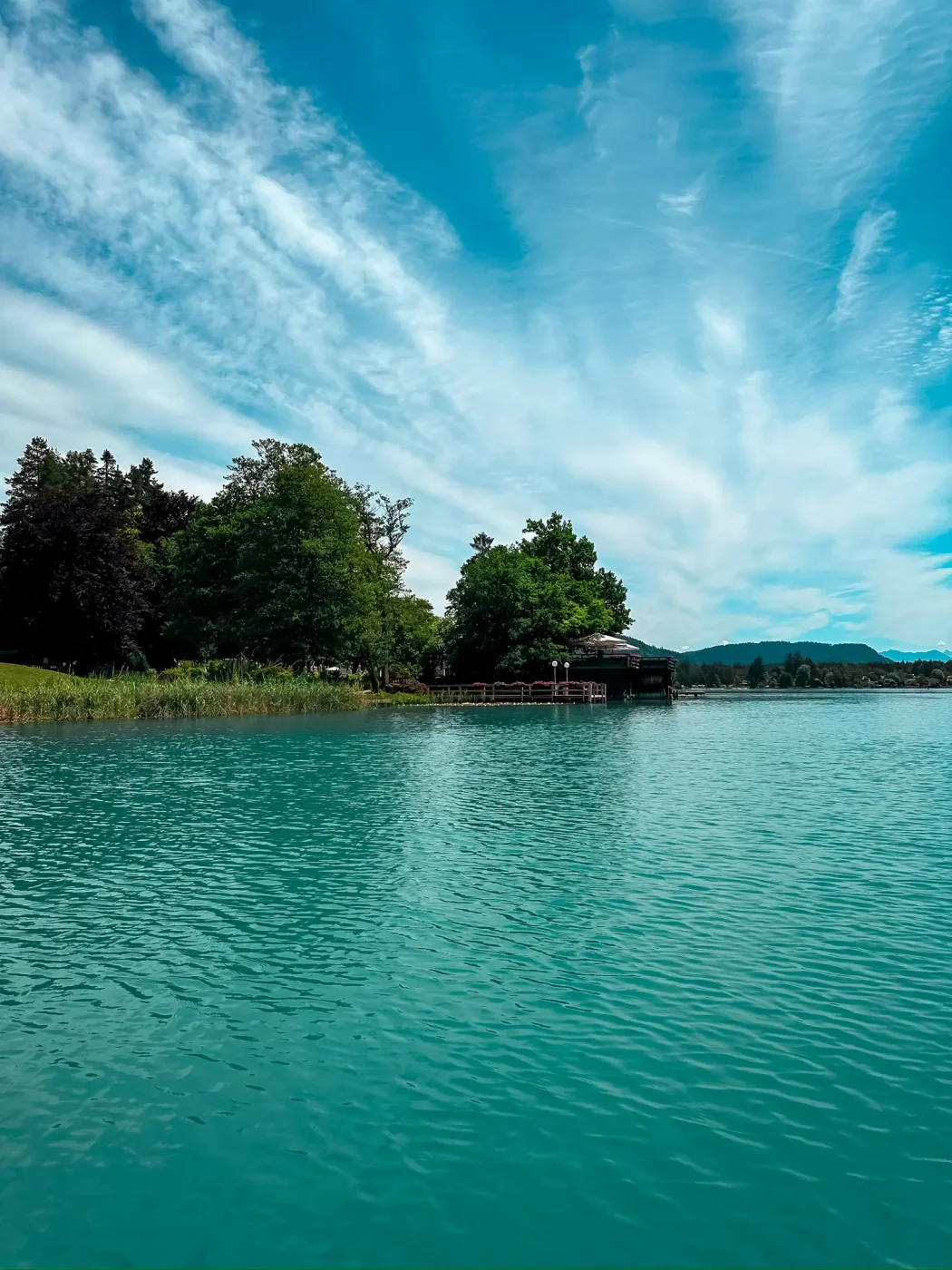 Blick über das türkisfarbene Wasser des Faaker Sees mit bewaldetem Ufer