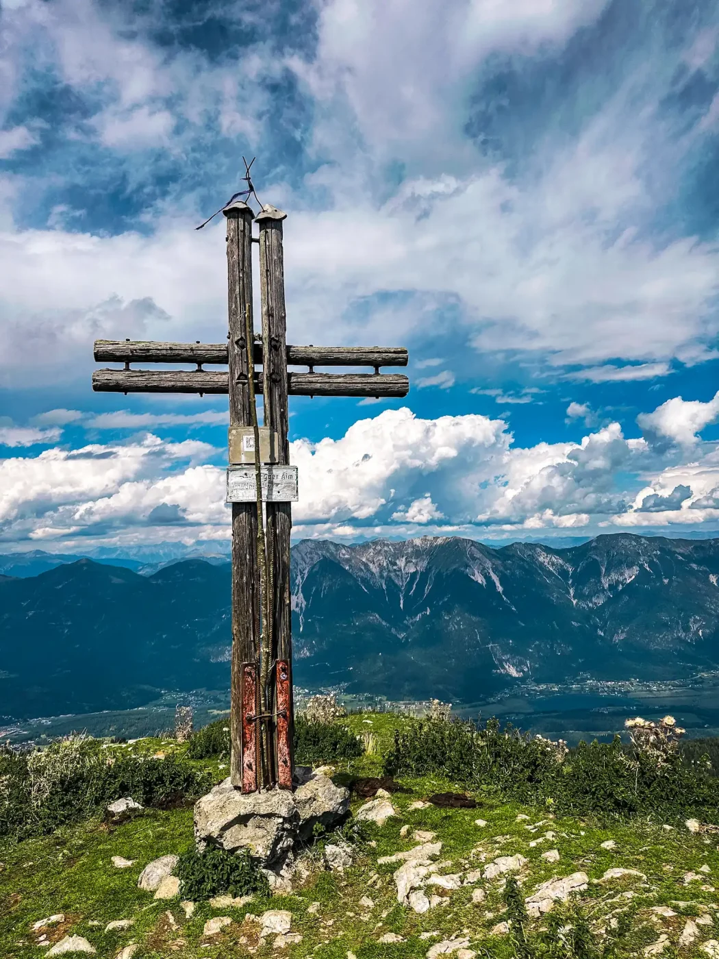 Blick auf das Gipfelkreuz des Poludnig mit Bergkette im Hintergrund